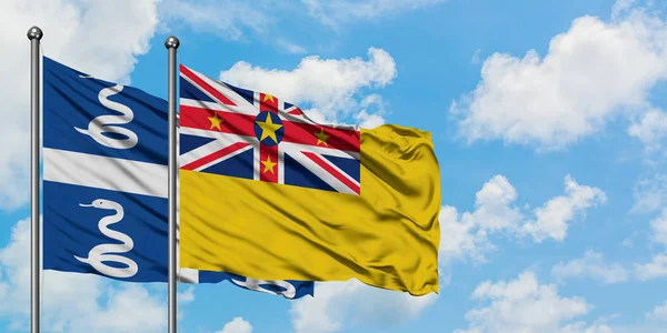Martinica y la bandera de Niue ondeando en el viento contra el cielo azul nublado blanco juntos. Concepto diplomático, relaciones internacionales . — Foto de Stock