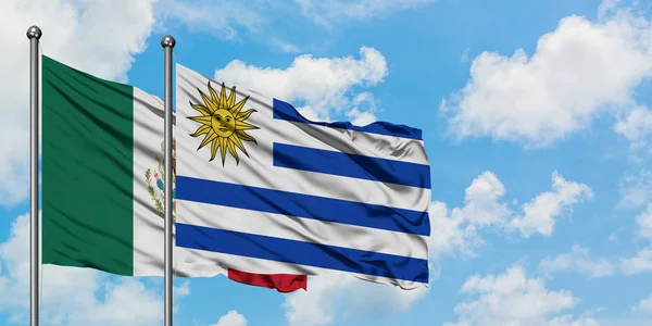 Η σημαία του Μεξικού και της Ουρουγουάης κουνώντας τον άνεμο εναντίον του λευκού νεφελώδη μπλε ουρανού μαζί. Φιλοσοφία της διπλωματίας, διεθνείς σχέσεις. — Φωτογραφία Αρχείου
