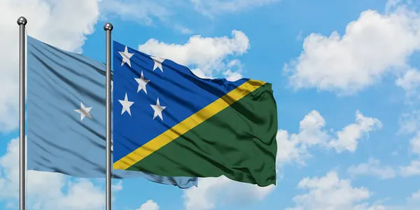 Bandera de Micronesia y las Islas Salomón ondeando en el viento contra el cielo azul nublado blanco juntos. Concepto diplomático, relaciones internacionales . — Foto de Stock