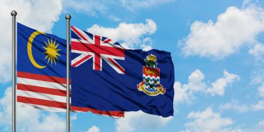 Malezya ve Cayman Adaları bayrağı birlikte beyaz bulutlu mavi gökyüzüne karşı rüzgarsal sallayarak. Diplomasi kavramı, uluslararası ilişkiler.