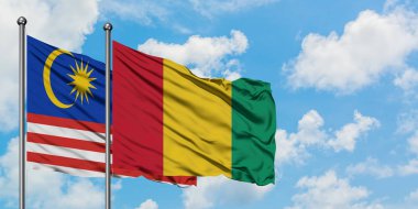 Malezya ve Gine bayrağı birlikte beyaz bulutlu mavi gökyüzüne karşı rüzgarsal sallayarak. Diplomasi kavramı, uluslararası ilişkiler.