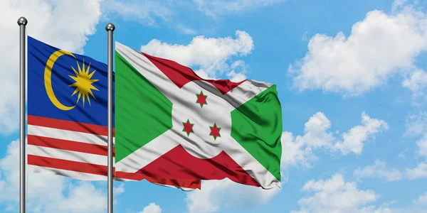 Bandera de Malasia y Burundi ondeando en el viento contra el cielo azul nublado blanco juntos. Concepto diplomático, relaciones internacionales . — Foto de Stock