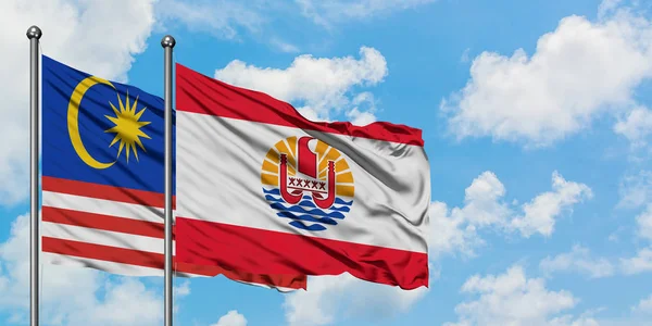 Malaien und Französisch-Polynesien schwenken gemeinsam die Flagge im Wind vor dem wolkenverhangenen blauen Himmel. Diplomatie-Konzept, internationale Beziehungen. — Stockfoto