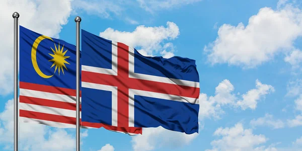 Bandera de Malasia e Islandia ondeando en el viento contra el cielo azul nublado blanco juntos. Concepto diplomático, relaciones internacionales . — Foto de Stock