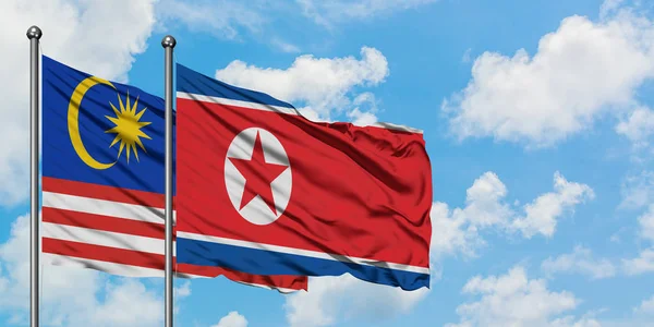 Флаг Малайзии и Северной Кореи, размахивающий на ветру против белого облачного голубого неба вместе взятого. Концепция дипломатии, международные отношения . — стоковое фото
