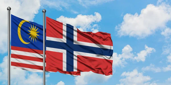 Malajsie a Norsko vlaje ve větru proti bíle zatažené modré obloze. Diplomacie, mezinárodní vztahy. — Stock fotografie