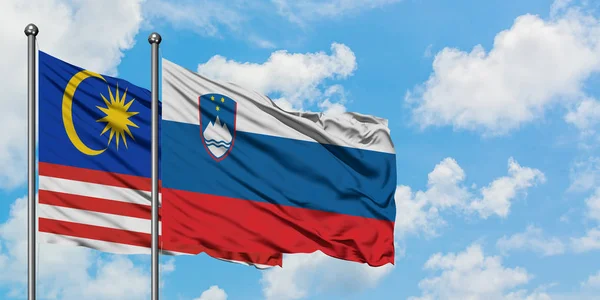 Malaysia and Slovenia flag waving in the wind against white cloudy blue sky together. Diplomacy concept, international relations.
