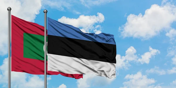 Maldivas y bandera de Estonia ondeando en el viento contra el cielo azul nublado blanco juntos. Concepto diplomático, relaciones internacionales . — Foto de Stock