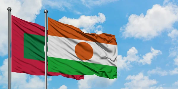 Maldivas y bandera de Níger ondeando en el viento contra el cielo azul nublado blanco juntas. Concepto diplomático, relaciones internacionales . — Foto de Stock