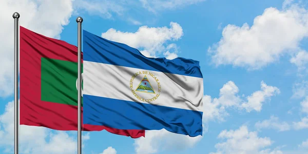 Maldivas y bandera de Nicaragua ondeando en el viento contra el cielo azul nublado blanco juntas. Concepto diplomático, relaciones internacionales . — Foto de Stock