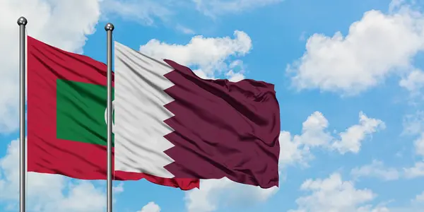 Maldivas y la bandera de Qatar ondeando en el viento contra el blanco cielo azul nublado juntos. Concepto diplomático, relaciones internacionales . — Foto de Stock