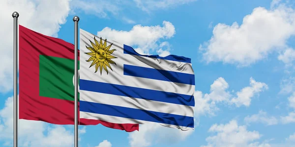 Maldivas y bandera de Uruguay ondeando en el viento contra el cielo azul nublado blanco juntos. Concepto diplomático, relaciones internacionales . — Foto de Stock