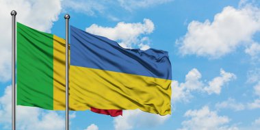 Mali ve Ukrayna bayrağı birlikte beyaz bulutlu mavi gökyüzüne karşı rüzgarda sallayarak. Diplomasi kavramı, uluslararası ilişkiler.