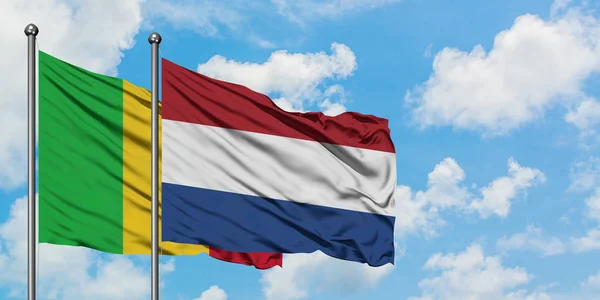 Bandiera del Mali e dei Paesi Bassi sventola nel vento contro il bianco cielo blu nuvoloso insieme. Concetto di diplomazia, relazioni internazionali . — Foto Stock