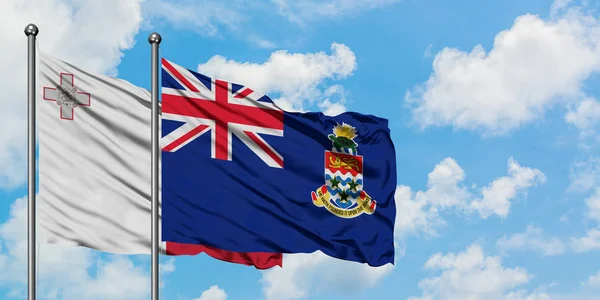 Malta och Cayman öarna flagga vinka i vinden mot vit grumlig blå himmel tillsammans. Diplomatisk koncept, internationella relationer. — Stockfoto