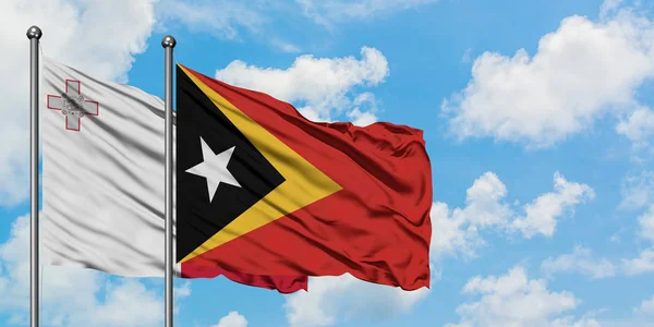 Bandera de Malta y Timor Oriental ondeando en el viento contra el cielo azul nublado blanco juntos. Concepto diplomático, relaciones internacionales . —  Fotos de Stock