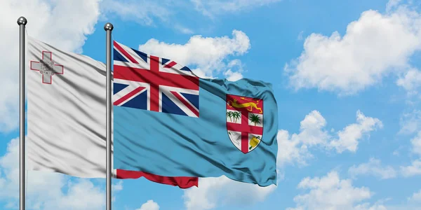 Bandera de Malta y Fiyi ondeando en el viento contra el cielo azul nublado blanco juntos. Concepto diplomático, relaciones internacionales . — Foto de Stock