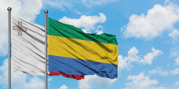 Bandera de Malta y Gabón ondeando en el viento contra el cielo azul nublado blanco juntos. Concepto diplomático, relaciones internacionales . — Foto de Stock