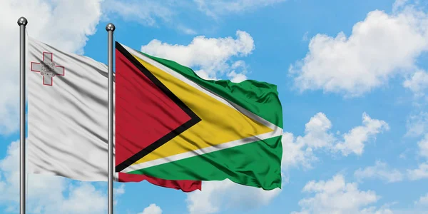 Bandera de Malta y Guyana ondeando en el viento contra el cielo azul nublado blanco juntos. Concepto diplomático, relaciones internacionales . — Foto de Stock