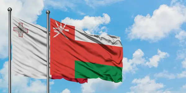 Bandera de Malta y Omán ondeando en el viento contra el cielo azul nublado blanco juntos. Concepto diplomático, relaciones internacionales . — Foto de Stock