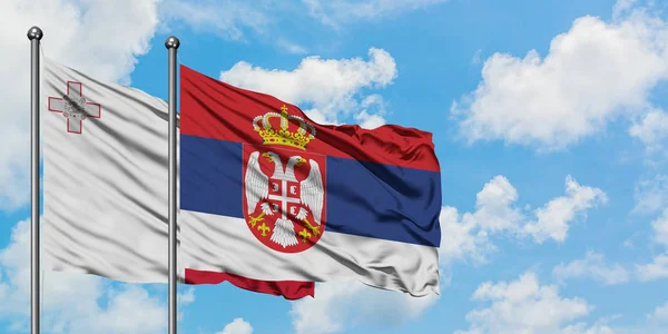 Bandera de Malta y Serbia ondeando en el viento contra el cielo azul nublado blanco juntos. Concepto diplomático, relaciones internacionales . — Foto de Stock