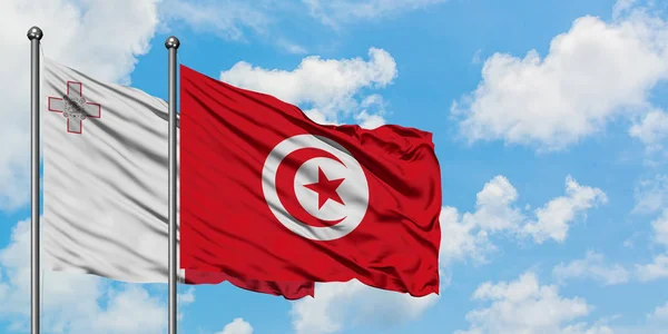 Malta och Tunisien flagga vifta i vinden mot vit grumlig blå himmel tillsammans. Diplomatisk koncept, internationella relationer. — Stockfoto