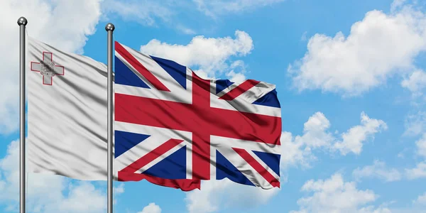 Malta och Storbritannien sjunker vifta i vinden mot vit grumlig blå himmel tillsammans. Diplomatisk koncept, internationella relationer. — Stockfoto