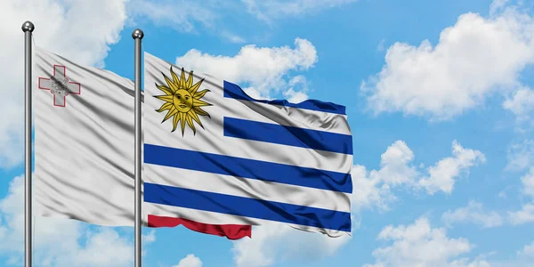 Bandera de Malta y Uruguay ondeando en el viento contra el cielo azul nublado blanco juntos. Concepto diplomático, relaciones internacionales . — Foto de Stock