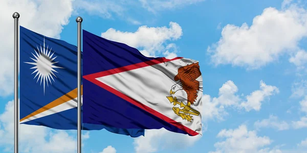 Ilhas Marshall e bandeira Samoa Americana agitando no vento contra o céu azul nublado branco juntos. Conceito de diplomacia, relações internacionais . — Fotografia de Stock