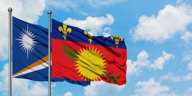 Marshall Adaları ve Guadeloupe bayrağı birlikte beyaz bulutlu mavi gökyüzüne karşı rüzgarda sallayarak. Diplomasi kavramı, uluslararası ilişkiler.