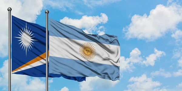 Bandera de las Islas Marshall y Argentina ondeando en el viento contra el cielo azul nublado blanco juntos. Concepto diplomático, relaciones internacionales . — Foto de Stock