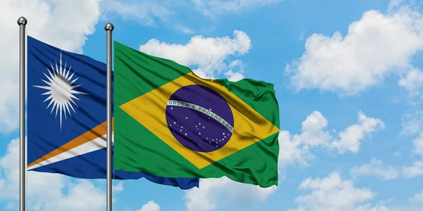 Bandera de las Islas Marshall y Brasil ondeando en el viento contra el cielo azul nublado blanco juntos. Concepto diplomático, relaciones internacionales . —  Fotos de Stock