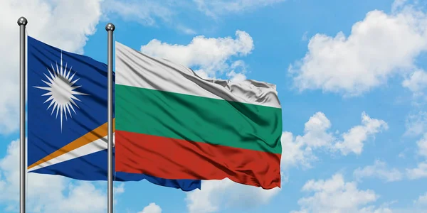 Bandera de las Islas Marshall y Bulgaria ondeando en el viento contra el cielo azul nublado blanco juntos. Concepto diplomático, relaciones internacionales . — Foto de Stock