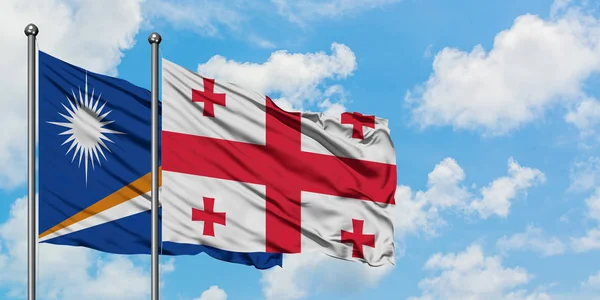 Bandera de las Islas Marshall y Georgia ondeando en el viento contra el cielo azul nublado blanco juntos. Concepto diplomático, relaciones internacionales . — Foto de Stock