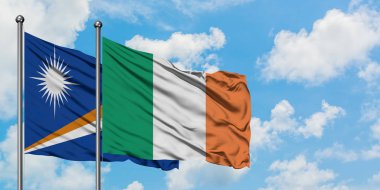 Marshall Adaları ve İrlanda bayrağı birlikte beyaz bulutlu mavi gökyüzüne karşı rüzgarda sallayarak. Diplomasi kavramı, uluslararası ilişkiler.