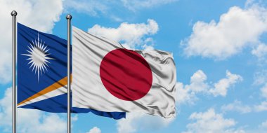 Marshall Adaları ve Japonya bayrağı birlikte beyaz bulutlu mavi gökyüzüne karşı rüzgarda sallayarak. Diplomasi kavramı, uluslararası ilişkiler.