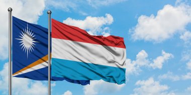 Marshall Adaları ve Lüksemburg bayrağı birlikte beyaz bulutlu mavi gökyüzüne karşı rüzgarda sallayarak. Diplomasi kavramı, uluslararası ilişkiler.