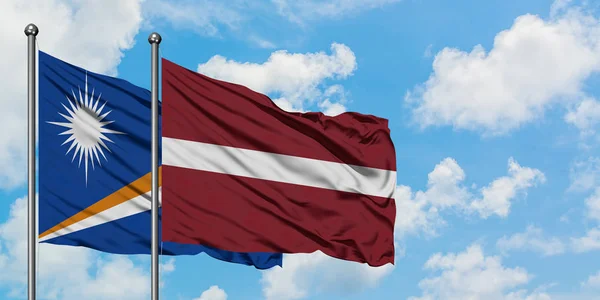 一緒に白い曇り青い空に対して風に振るマーシャル諸島とラトビアの旗。外交概念、国際関係. — ストック写真