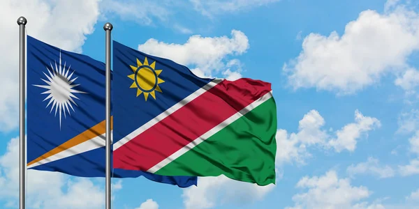 Drapeau des Îles Marshall et de la Namibie agitant dans le vent contre un ciel bleu nuageux blanc. Concept de diplomatie, relations internationales . — Photo