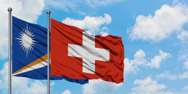 Marshall Adaları ve İsviçre bayrağı birlikte beyaz bulutlu mavi gökyüzüne karşı rüzgarda sallayarak. Diplomasi kavramı, uluslararası ilişkiler.