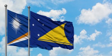 Marshall Adaları ve Tokelau bayrağı birlikte beyaz bulutlu mavi gökyüzüne karşı rüzgarda sallayarak. Diplomasi kavramı, uluslararası ilişkiler.