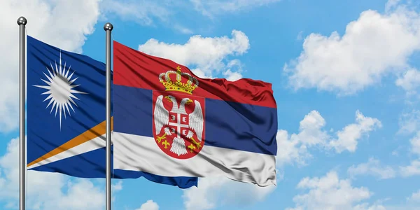 Bandera de las Islas Marshall y Serbia ondeando en el viento contra el cielo azul nublado blanco juntos. Concepto diplomático, relaciones internacionales . — Foto de Stock