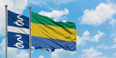 Martinik ve Gabon bayrağı birlikte beyaz bulutlu mavi gökyüzüne karşı rüzgarda sallayarak. Diplomasi kavramı, uluslararası ilişkiler.