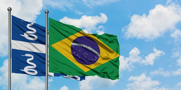 Martinica e a bandeira do Brasil agitando no vento contra o céu azul nublado branco juntos. Conceito de diplomacia, relações internacionais . — Fotografia de Stock