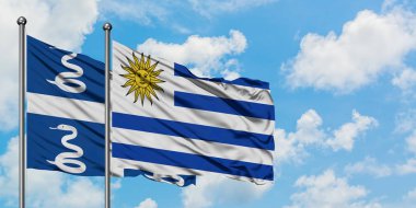 Martinik ve Uruguay bayrağı birlikte beyaz bulutlu mavi gökyüzüne karşı rüzgarda sallayarak. Diplomasi kavramı, uluslararası ilişkiler.