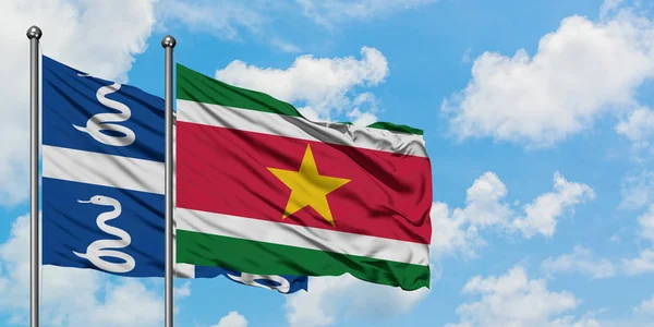 Bandera de Martinica y Surinam ondeando en el viento contra el cielo azul nublado blanco juntos. Concepto diplomático, relaciones internacionales . — Foto de Stock