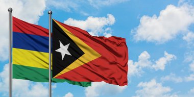 Mauritius ve Doğu Timor bayrağı birlikte beyaz bulutlu mavi gökyüzüne karşı rüzgarda sallayarak. Diplomasi kavramı, uluslararası ilişkiler.