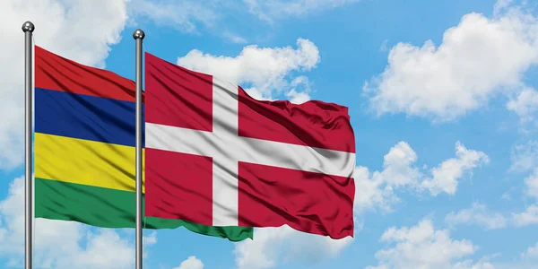Mauricius a Dánská vlajka mávali ve větru proti bíle zatažené modré obloze. Diplomacie, mezinárodní vztahy. — Stock fotografie