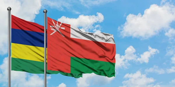 Bandera de Mauricio y Omán ondeando en el viento contra el cielo azul nublado blanco juntos. Concepto diplomático, relaciones internacionales . — Foto de Stock