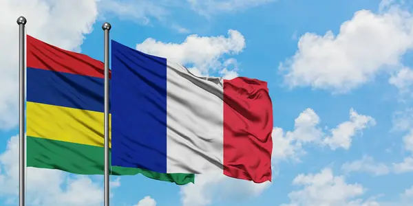 Mauricio y la bandera de Reunión ondeando en el viento contra el cielo azul nublado blanco juntos. Concepto diplomático, relaciones internacionales . — Foto de Stock